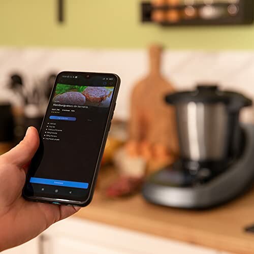 Persoon houdt smartphone vast in keuken met kookapparaat